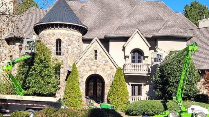 Stone-and-stucco home with a turret and arched entry, with shrubs trimmed beside the front walk